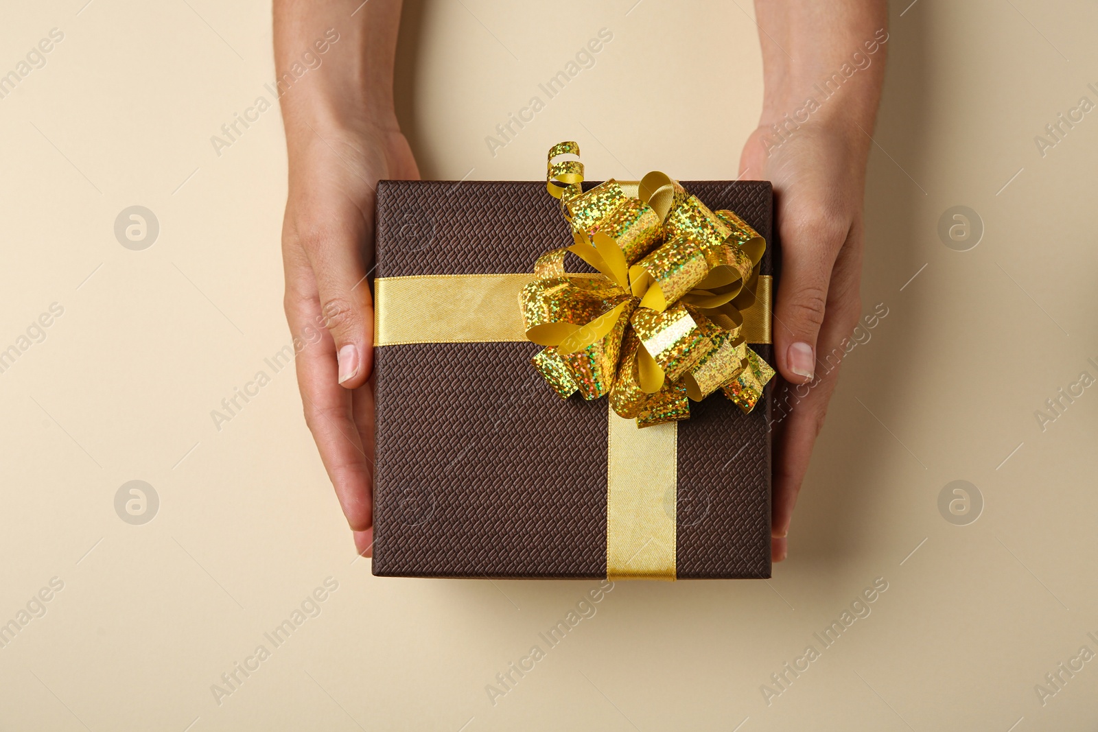 Photo of Woman holding beautiful gift box on beige background, top view