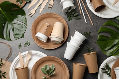 Photo of Flat lay composition with disposable tableware and different green leaves on grey background