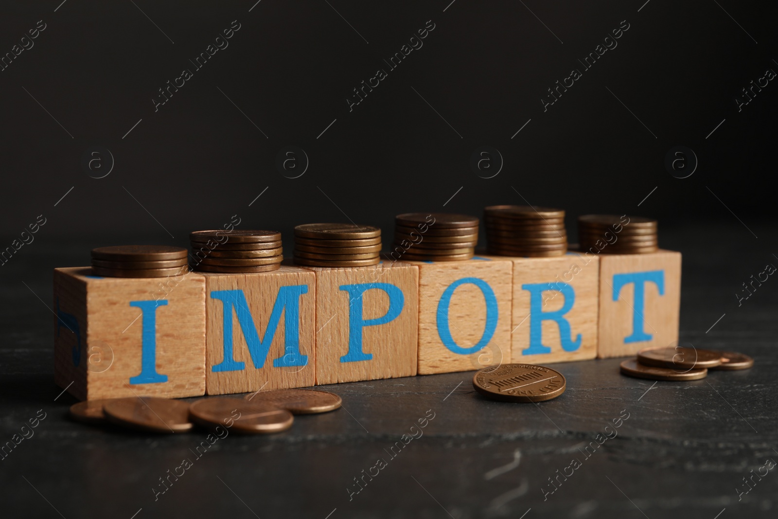 Photo of Word Import made of wooden cubes with letters and coins on black table, closeup