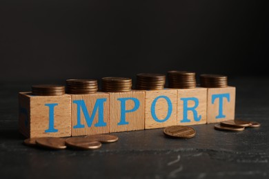 Photo of Word Import made of wooden cubes with letters and coins on black table, closeup