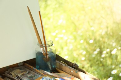 Photo of Easel with canvas and painting equipment outdoors, closeup