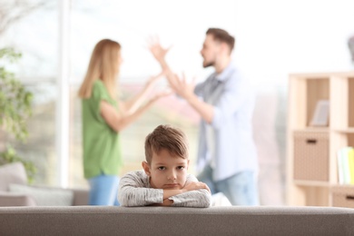 Little unhappy boy sitting on sofa while parents arguing at home