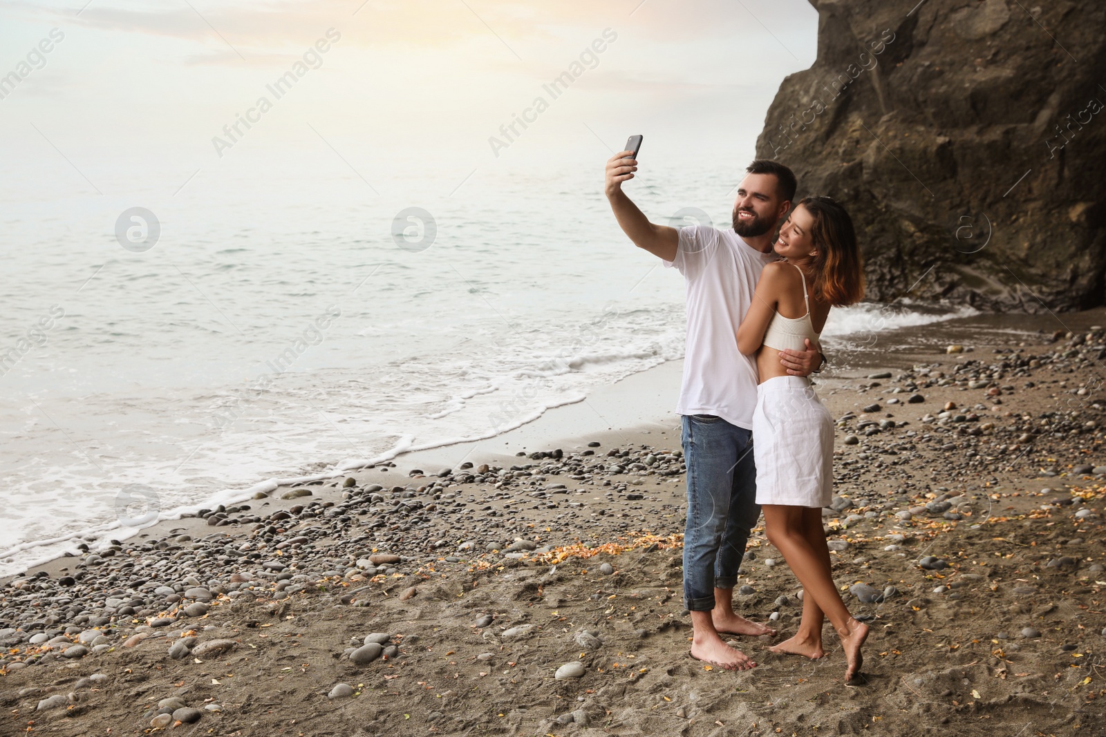 Photo of Happy young couple taking selfie on beach near sea. Space for text