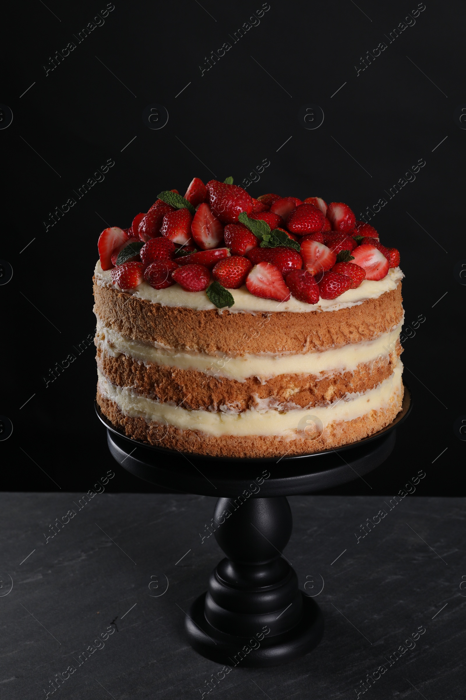 Photo of Tasty cake with fresh strawberries and mint on dark gray table against black background