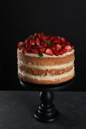 Tasty cake with fresh strawberries and mint on dark gray table against black background