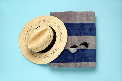 Photo of Beach towel, hat and sunglasses on light blue background, flat lay
