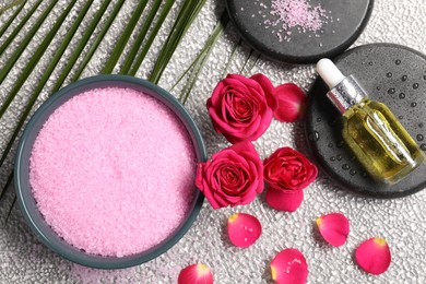 Natural sea salt in bowl, spa stones, cosmetic product, rose flowers and petals on grey table, flat lay