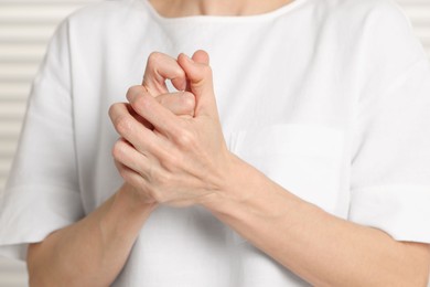 Woman cracking her knuckles on blurred background, closeup. Bad habit