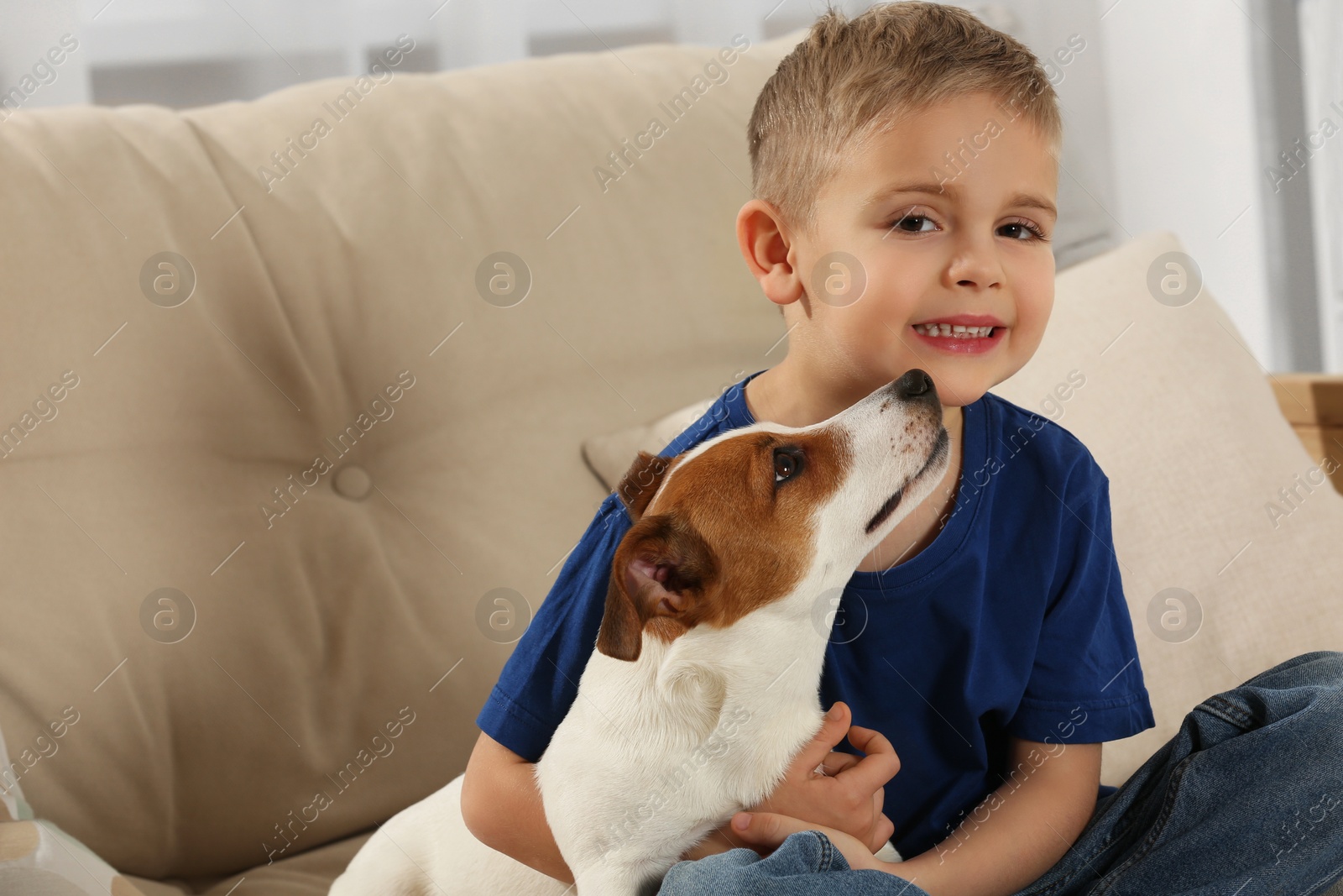 Photo of Little boy with his cute dog on sofa at home, space for text. Adorable pet