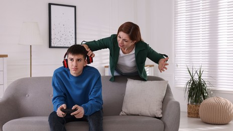 Photo of Mother scolding her son while he playing videogame at home. Teenager problems