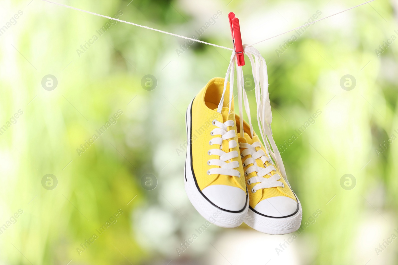 Photo of Stylish sneakers drying on washing line against blurred background