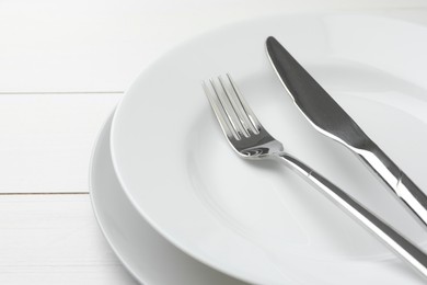Photo of Clean plates, fork and knife on white wooden table, closeup