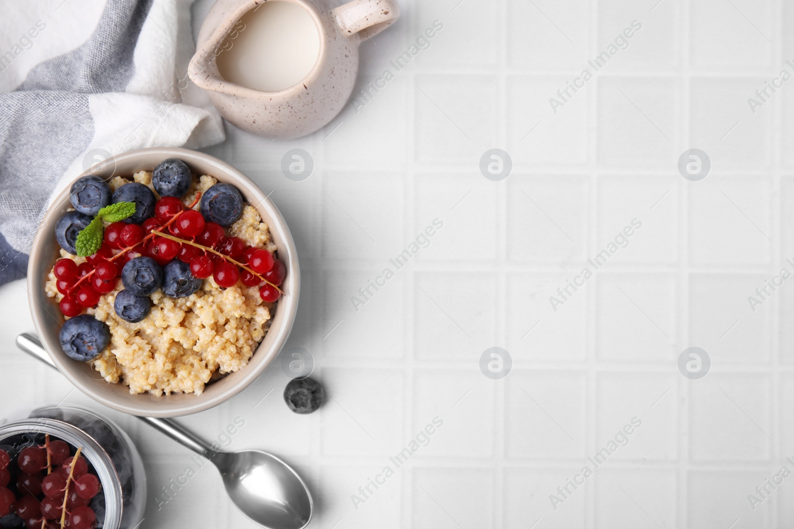 Photo of Bowl of delicious cooked quinoa with blueberries and cranberries on white tiled table, flat lay. Space for text