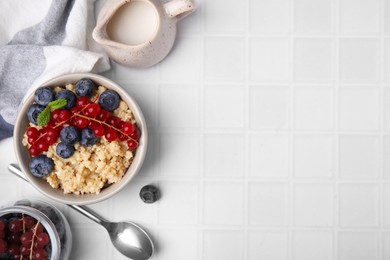 Bowl of delicious cooked quinoa with blueberries and cranberries on white tiled table, flat lay. Space for text