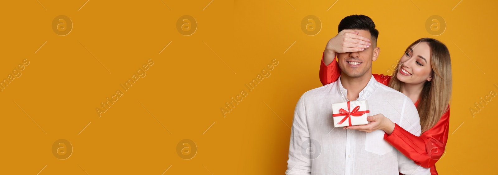 Image of Woman surprising her boyfriend with gift on yellow background, space for text. Valentine's Day banner design