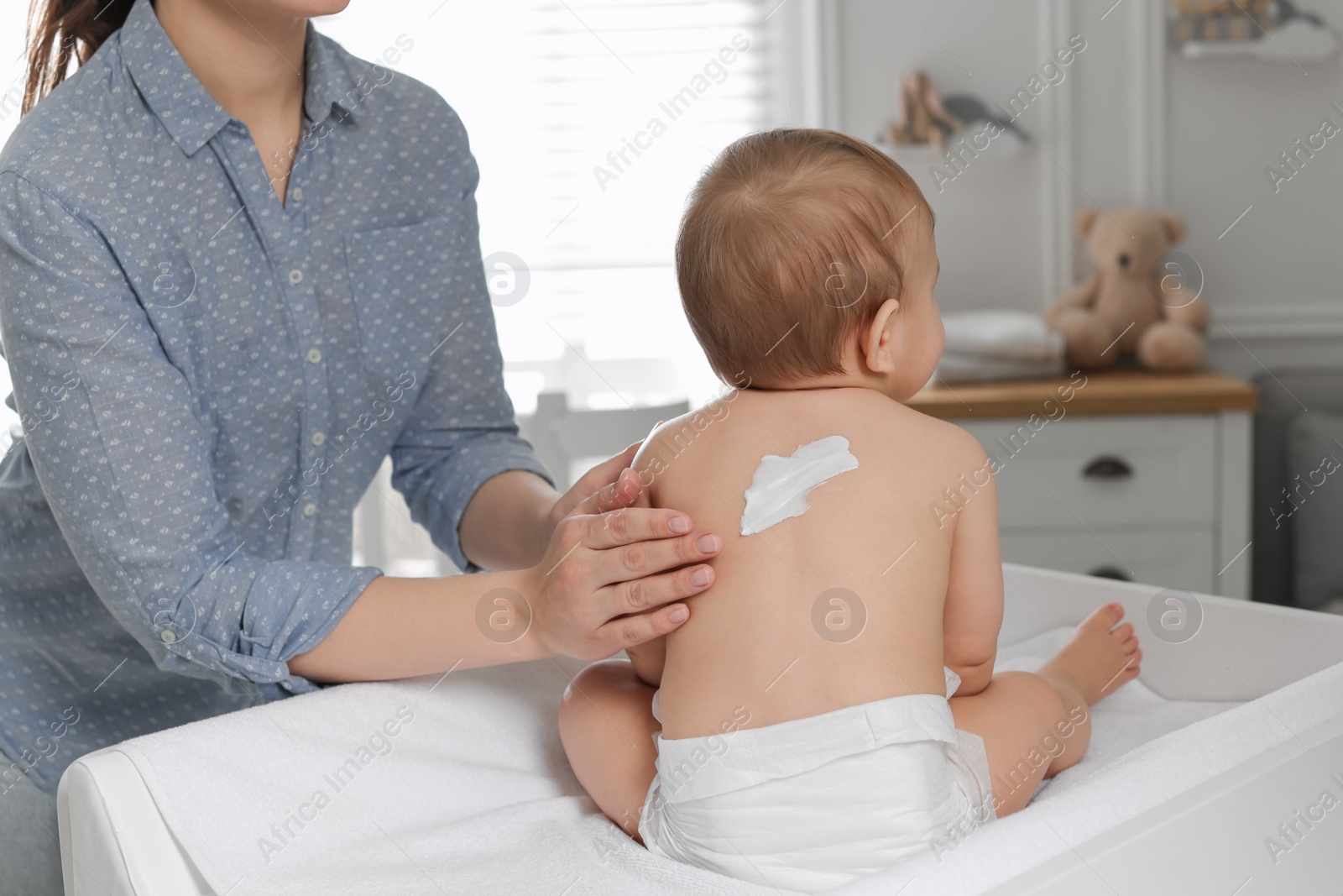 Photo of Mother applying body cream on her little baby at home, closeup