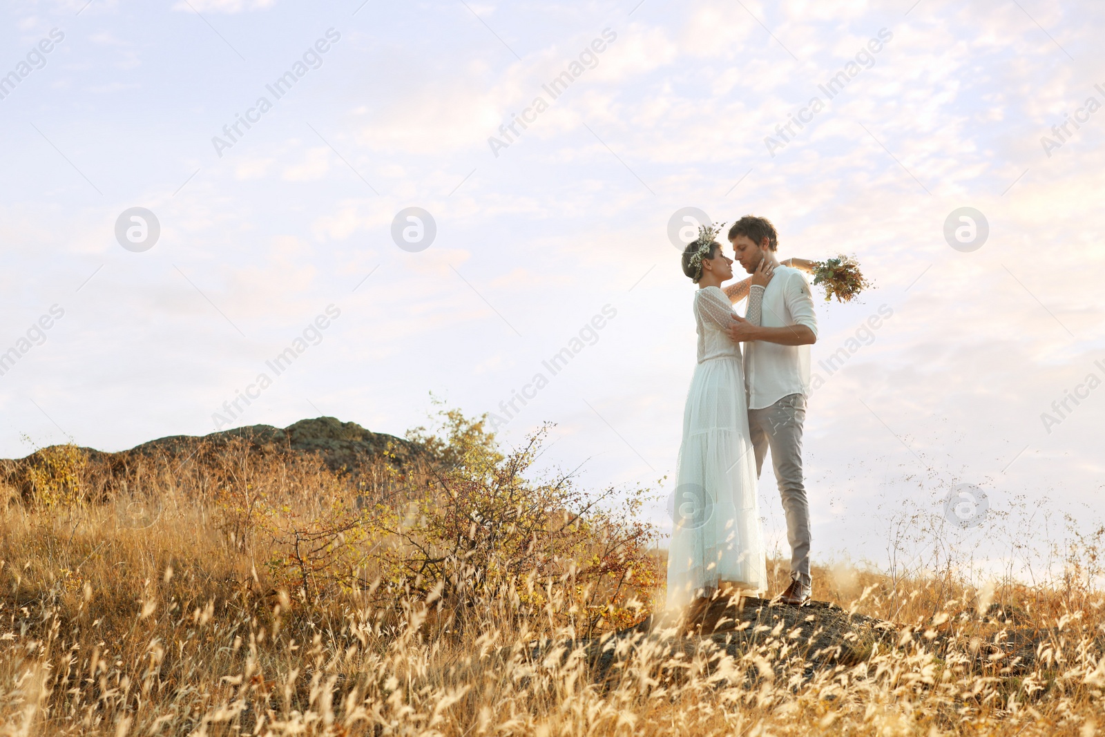 Photo of Happy newlyweds with beautiful field bouquet outdoors