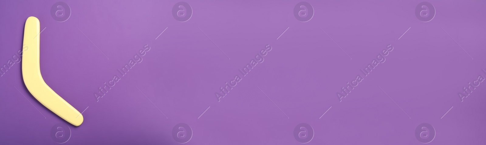 Photo of Yellow wooden boomerang on purple background, top view. Space for text