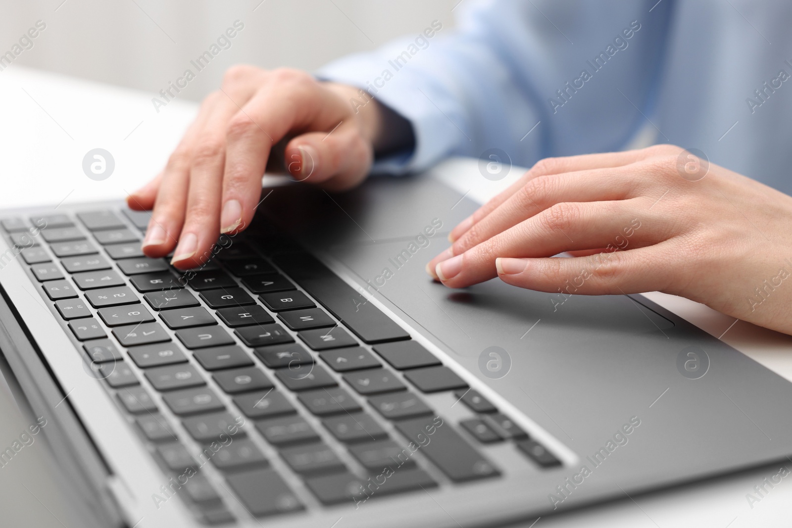 Photo of E-learning. Woman using laptop at white table indoors, closeup