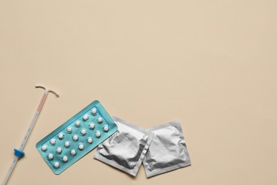 Contraception choice. Pills, condoms and intrauterine device on beige background, flat lay. Space for text