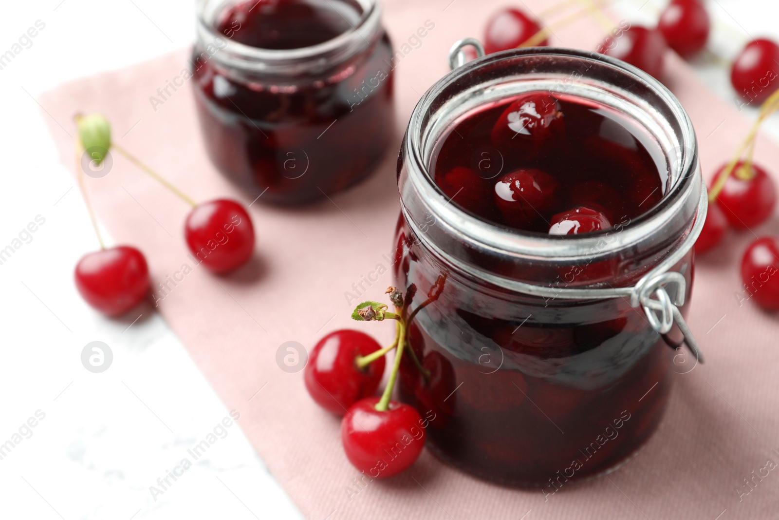 Photo of Jars of pickled cherries and fresh fruits on table, closeup