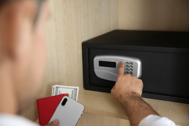 Photo of Man opening black steel safe with electronic lock at hotel, closeup