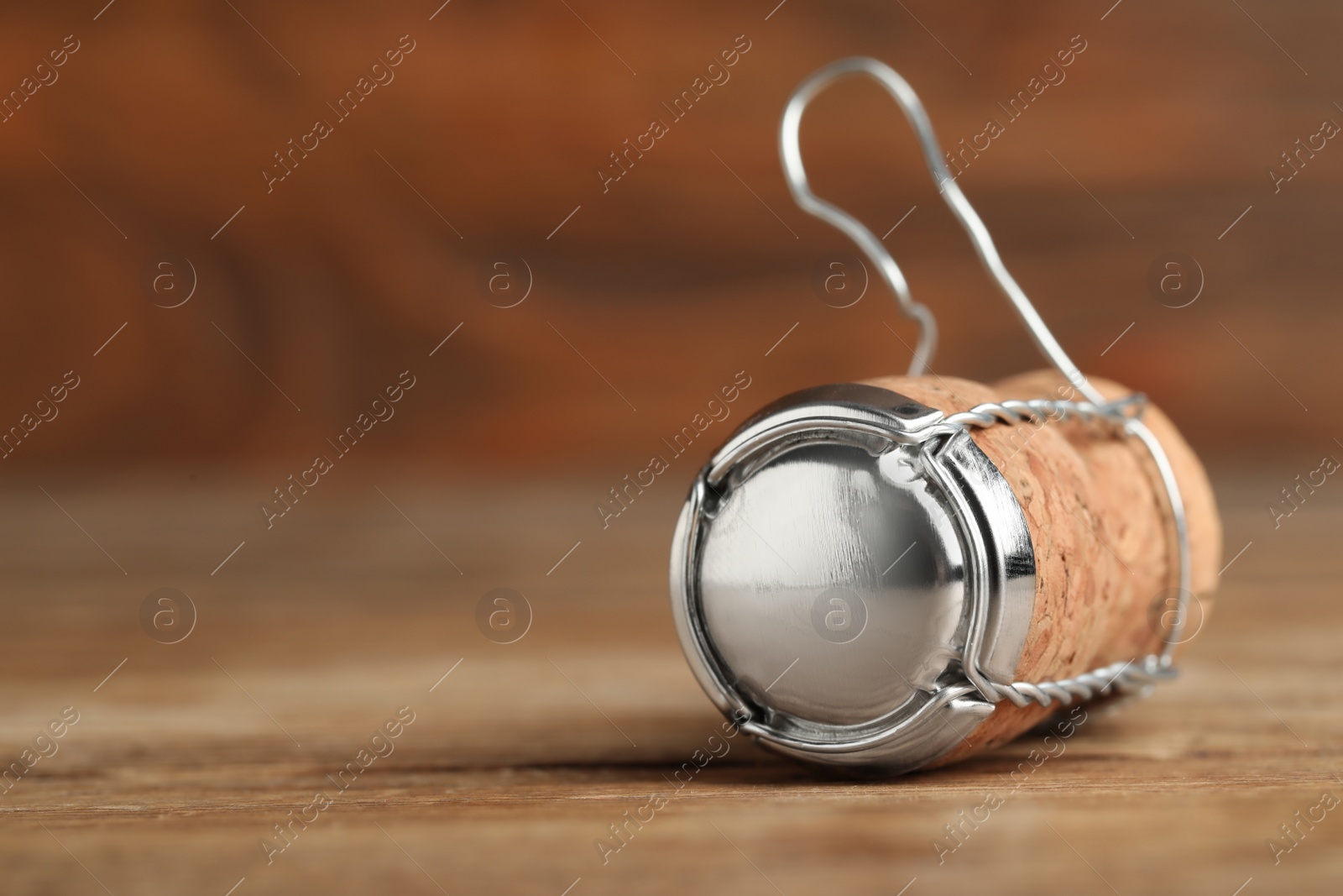 Photo of Sparkling wine cork with muselet cap on wooden table, closeup. Space for text