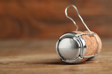 Photo of Sparkling wine cork with muselet cap on wooden table, closeup. Space for text