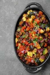 Dish with tasty ratatouille on grey textured table, top view