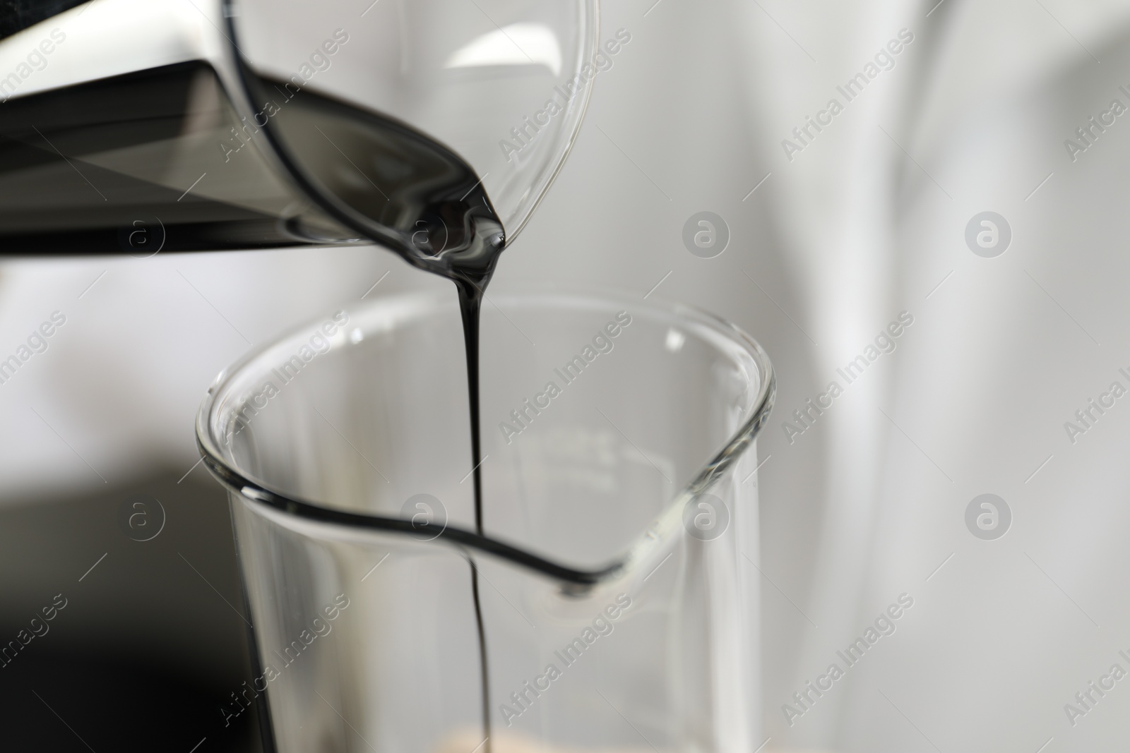 Photo of Pouring crude oil into beaker against blurred background, closeup