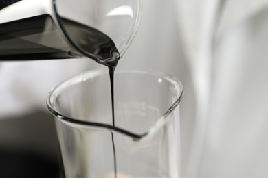 Pouring crude oil into beaker against blurred background, closeup