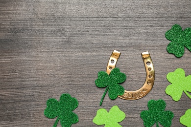 Photo of Golden horseshoe and decorative clover leaves on grey wooden table, flat lay with space for text. Saint Patrick's Day celebration