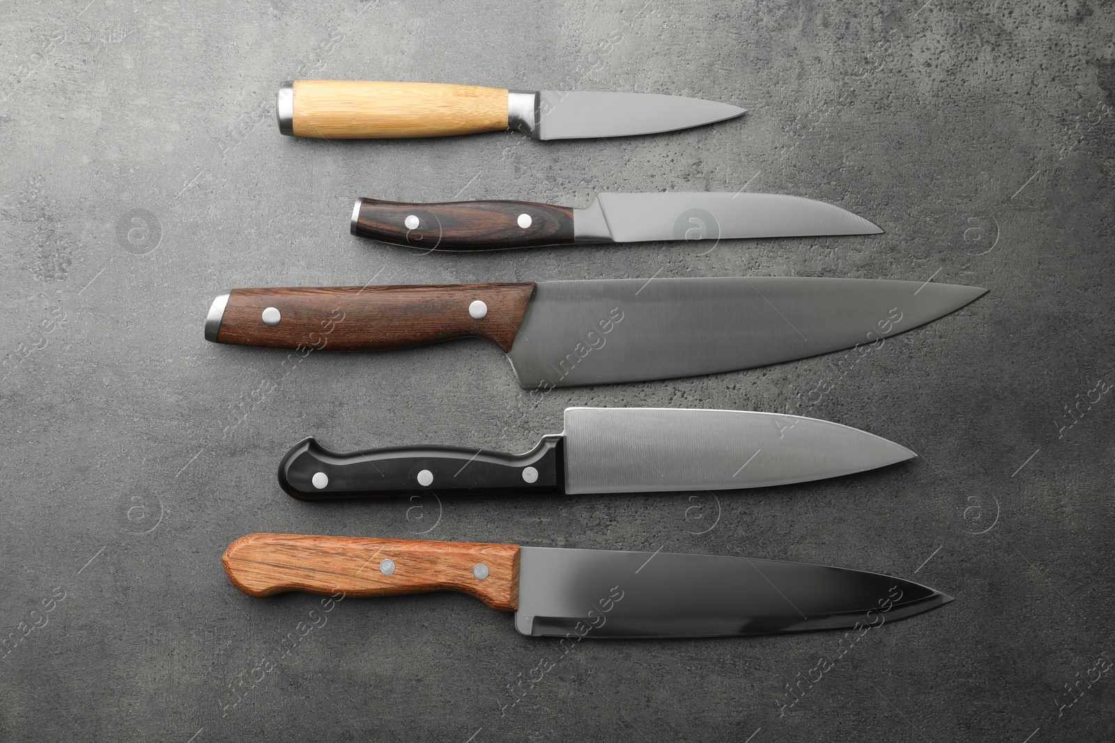 Photo of Many different knives on grey textured table, flat lay