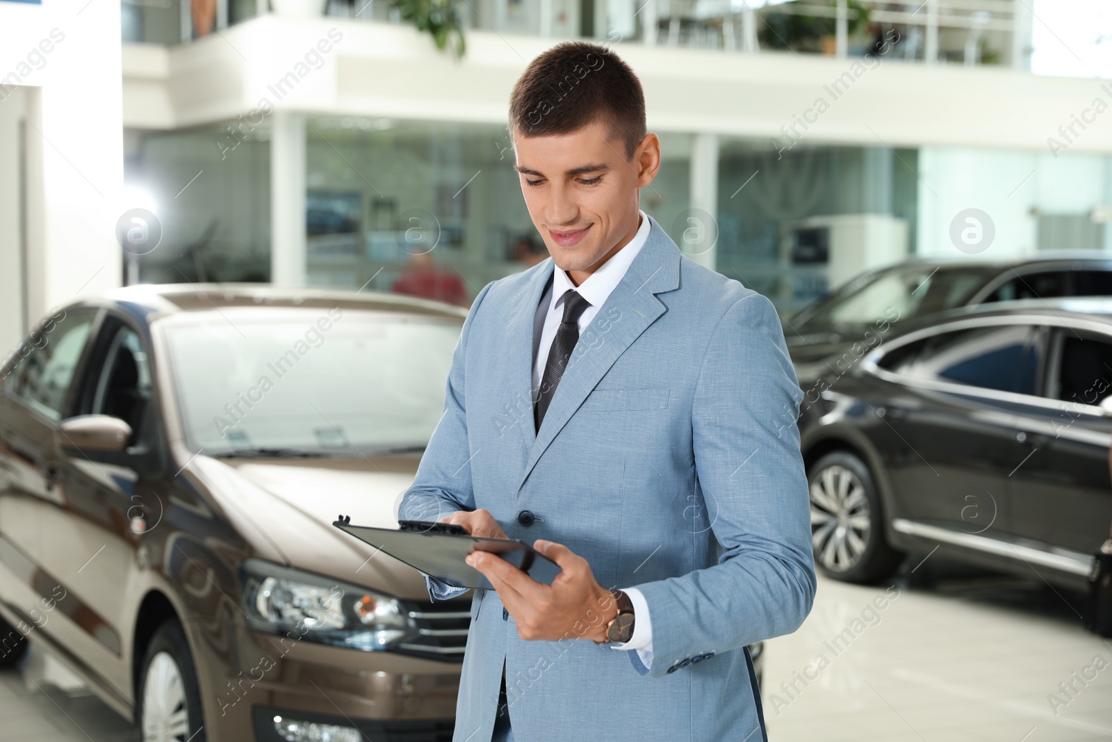 Photo of Young salesman with clipboard in modern car dealership