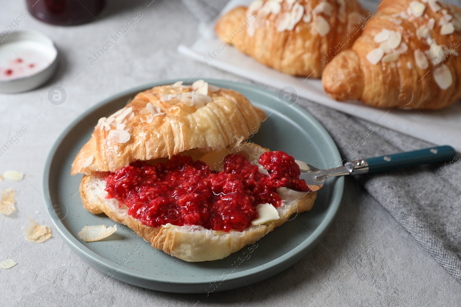 Photo of Delicious croissant with berry jam, butter and spoon on grey table