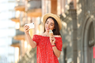 Happy young woman with delicious ice cream in waffle cone taking selfie outdoors