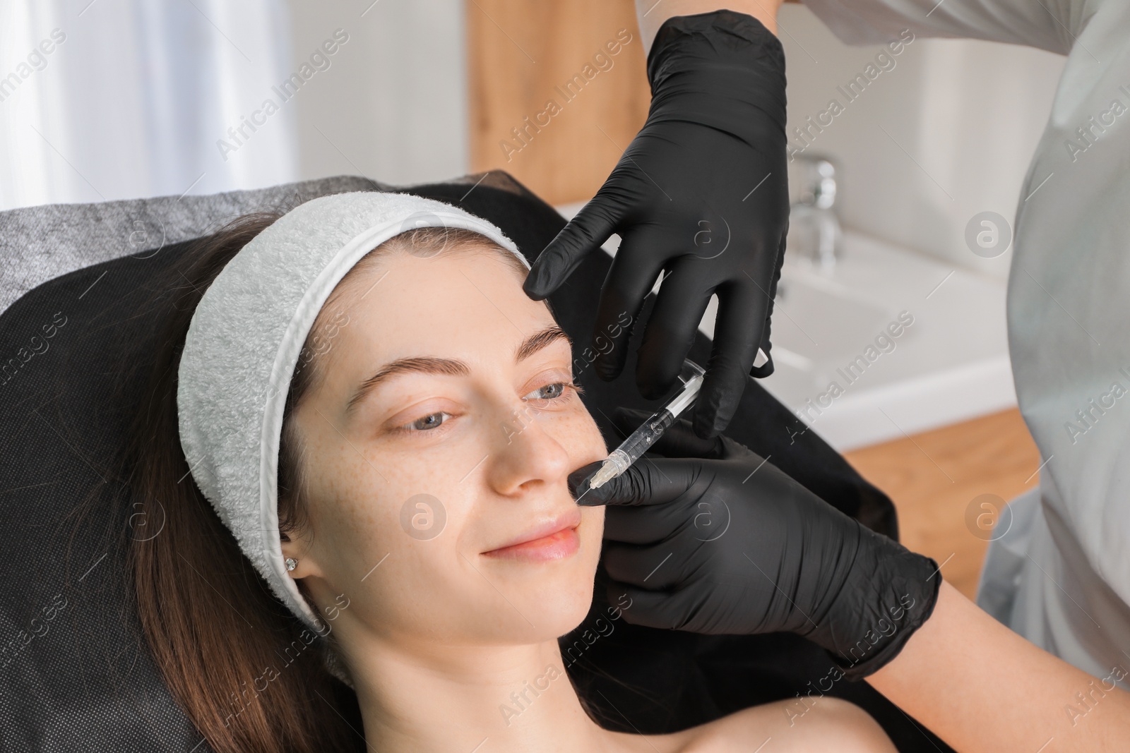 Photo of Cosmetologist giving lips injection to patient in clinic, closeup. Cosmetic surgery