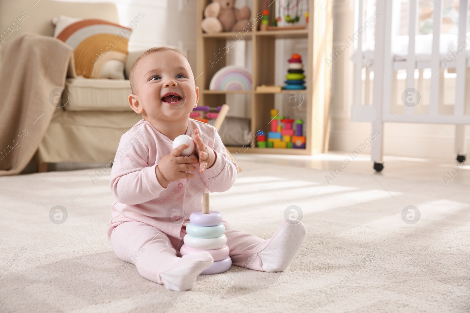 Photo of Cute baby girl playing with toy pyramid on floor at home
