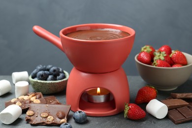 Fondue pot with melted chocolate, marshmallows and different fresh berries on grey table