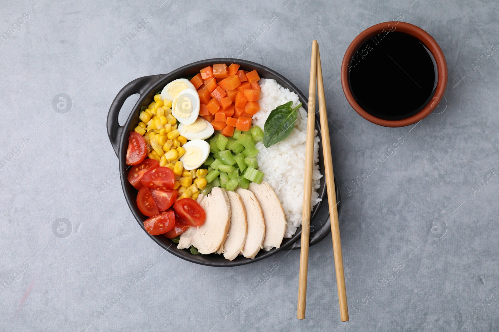 Photo of Delicious poke bowl with different ingredients, chopsticks and soy sauce on grey table, flat lay