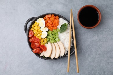 Delicious poke bowl with different ingredients, chopsticks and soy sauce on grey table, flat lay