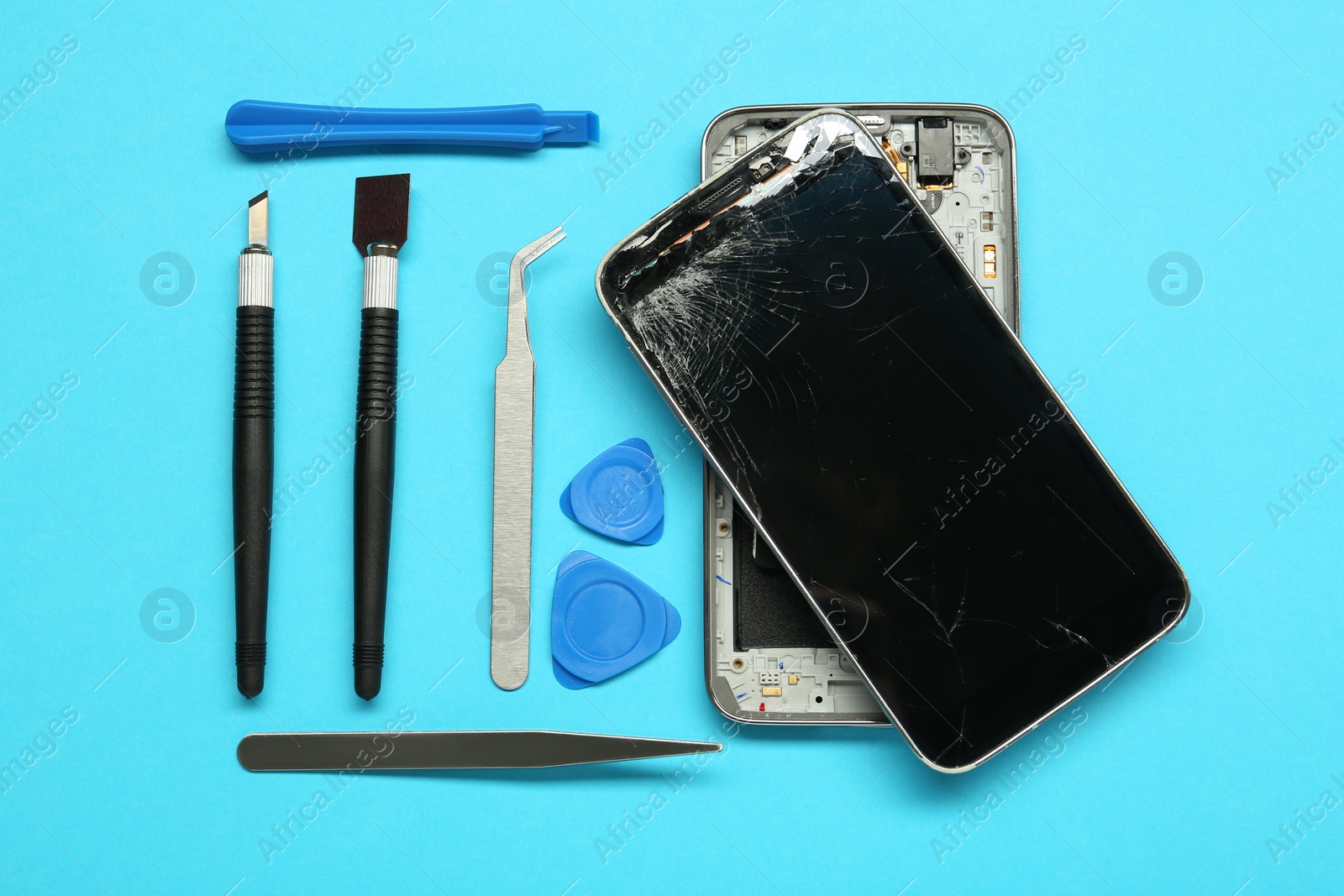 Photo of Damaged smartphone and repair tool set on light blue background, flat lay