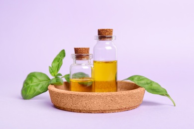 Photo of Plate with glass bottles of oil and basil leaves on color background