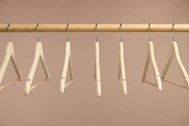 Photo of Empty clothes hangers on wooden rack against light brown background