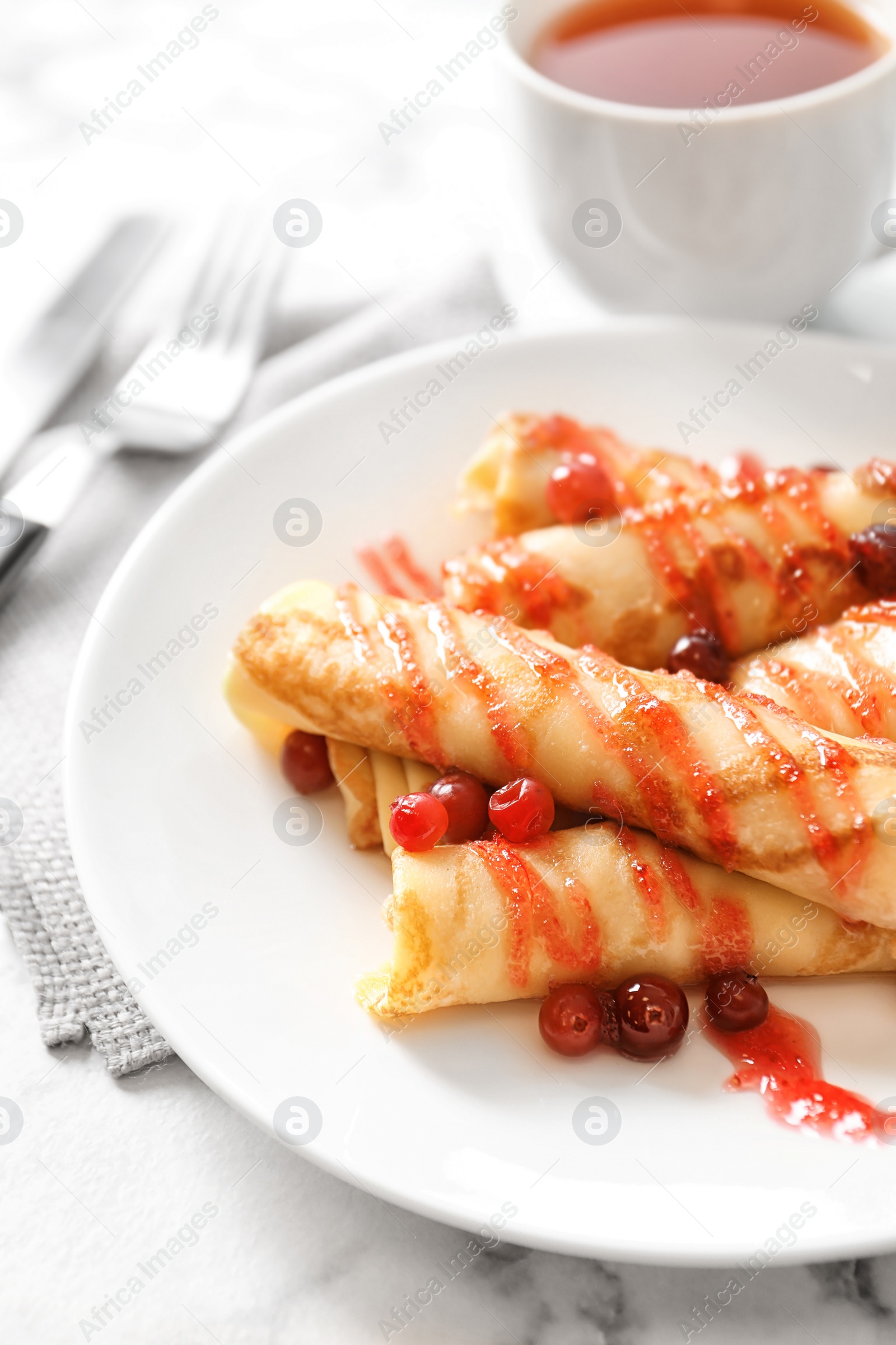 Photo of Thin pancakes with berries and syrup on plate, closeup