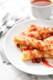 Photo of Thin pancakes with berries and syrup on plate, closeup