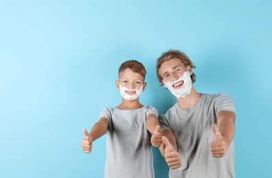 Father and son with shaving foam on faces against color background, space for text