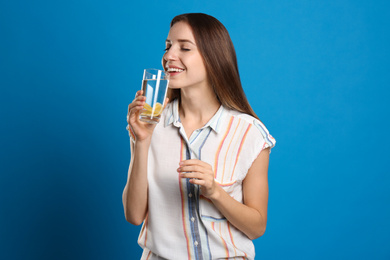 Young woman drinking lemon water on light blue background