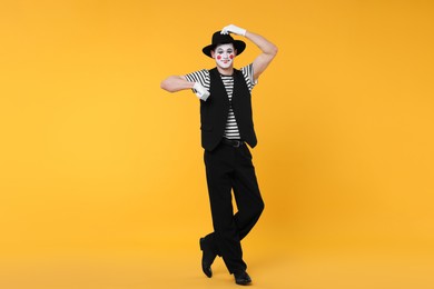 Photo of Funny mime artist in hat posing on orange background
