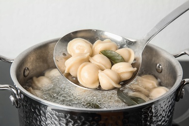 Closeup of dumplings on skimmer over stewpan with boiling water. Home cooking